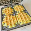 Four golden zucchini waffles cooking evenly inside a waffle maker.