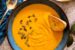 Creamy homemade pumpkin soup served in a bowl, topped with roasted pumpkin seeds and a drizzle of olive oil, with toasted bread in the background.