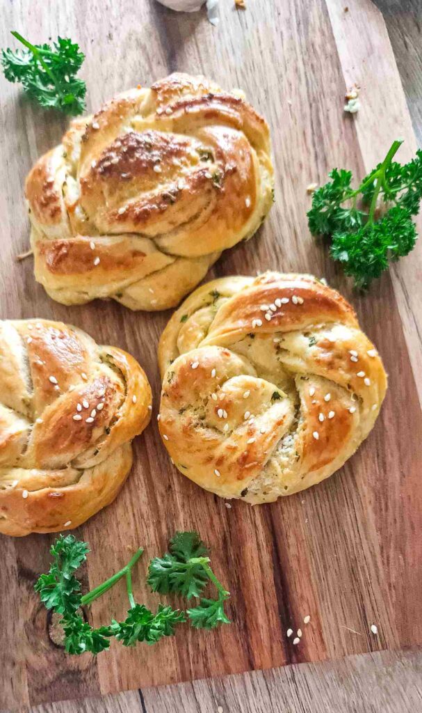 Golden-brown homemade garlic, cheese, and herb twists on a baking tray, topped with sesame seeds and freshly grated Parmesan, ready to serve as a snack or appetizer
