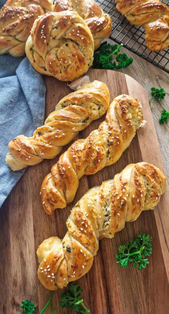 Golden-brown homemade garlic, cheese, and herb twists on a baking tray, topped with sesame seeds and freshly grated Parmesan, ready to serve as a snack or appetizer