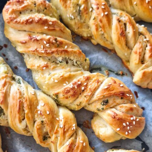 Golden-brown homemade garlic, cheese, and herb twists on a baking tray, topped with sesame seeds, freshly baked and ready to serve as a snack or appetizer.