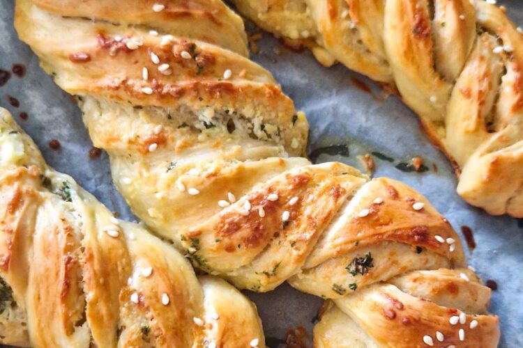 Golden-brown homemade garlic, cheese, and herb twists on a baking tray, topped with sesame seeds, freshly baked and ready to serve as a snack or appetizer.