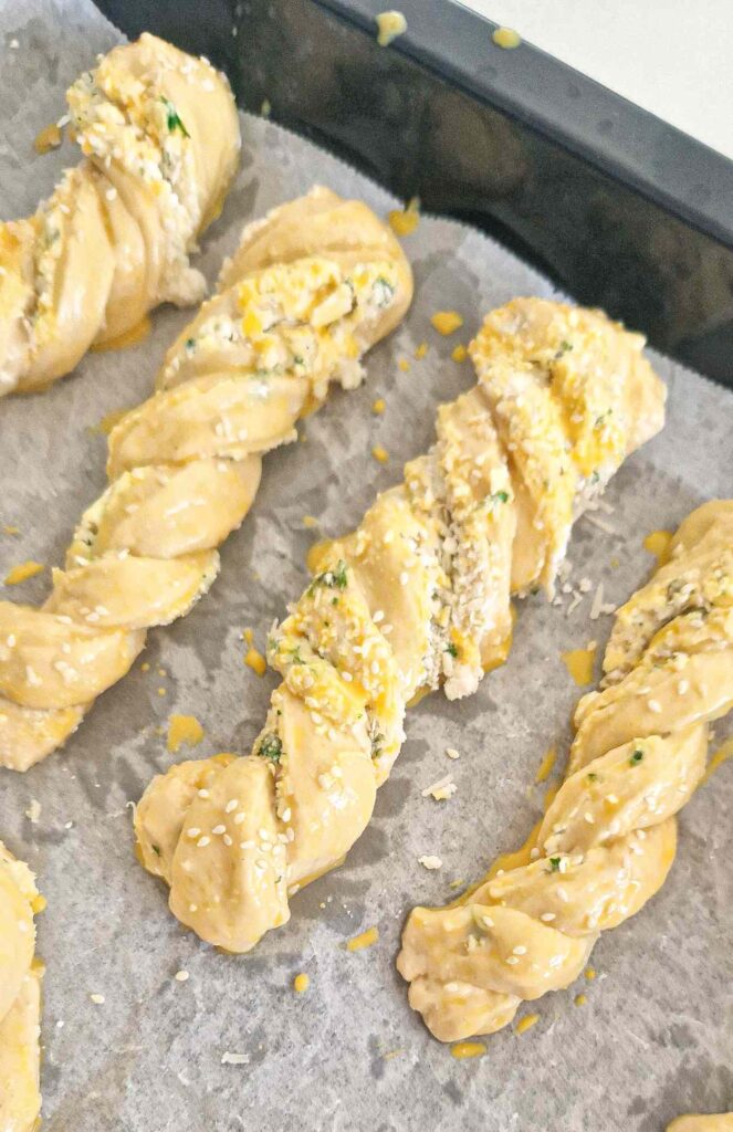 Homemade garlic, cheese, and herb twists arranged on a baking tray, brushed with egg wash, ready to go into the oven.