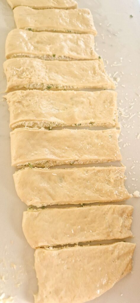 Rectangular homemade dough rolled out on a floured surface, ready to be spread with garlic, herb butter and cheese for making twists.