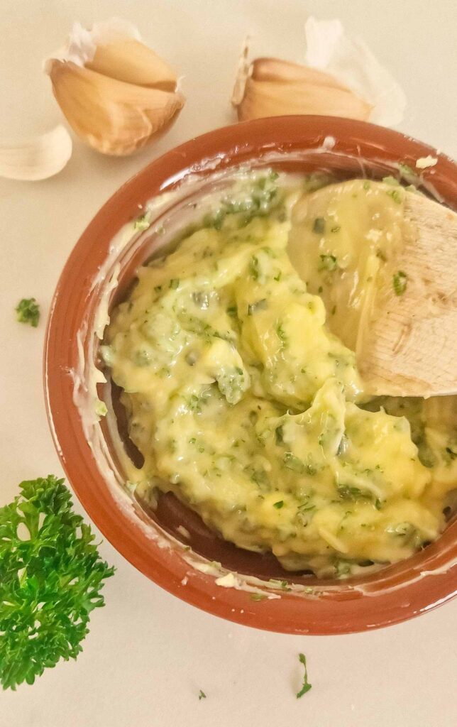 Small bowl of soft garlic and herb butter, mixed with minced garlic, chopped parsley, and rosemary, ready to be spread over homemade dough